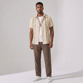 Man wearing a beige patterned shirt and pants on a gray background