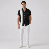 Man wearing a black and white shirt with white pants on a light gray background