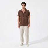 Man wearing a coffee patterned shirt and beige pants on a white background