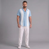 Man wearing a light blue and white striped shirt with white pants on a gray background