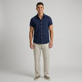 Man wearing a navy button-up shirt and beige striped pants on a gray background