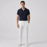 Man wearing a navy polo shirt and white pants on a light gray background
