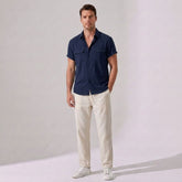 Man wearing a navy shirt and beige pants against a plain background