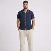 Man wearing a navy short-sleeve shirt and beige pants on a white background