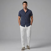 Man wearing a navy striped shirt and white pants on a gray background