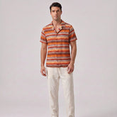 Man wearing a patterned shirt and light pants on a plain background