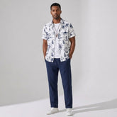 Man wearing a white patterned shirt and navy pants on a gray background