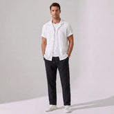 Man wearing a white shirt and black pants against a plain background