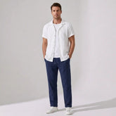 Man wearing a white shirt and navy pants against a plain background