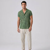 Man wearing green patterned short-sleeve Cuban shirt with white trousers