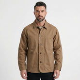 A man wearing a brown utility field jacket with four front pockets, shown against a plain light gray studio background.