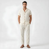 Man wearing a beige floral checkerboard jacquard Cuban shirt and straight leg linen pants front view on white background