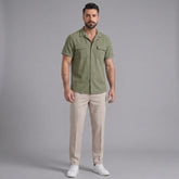 Man wearing a dark green linen Cuban collar shirt and slim fit tapered trousers front view on plain background