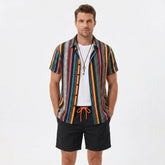 Man wearing a colorful ethnic geometric print button up shirt and swim shorts front view on plain background