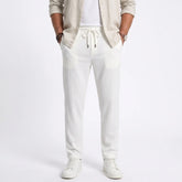 Man wearing MannerCo white jacquard ribbed straight leg drawstring trousers, front view on plain background