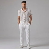 Man wearing a tan striped mesh Cuban shirt and beige linen pants on a light gray background