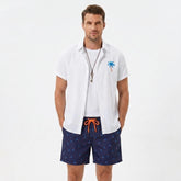 Man wearing a white palm tree print linen look cotton button up shirt and swim shorts front view on plain background