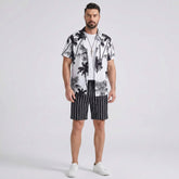 Man wearing a white palm trees print button up shirt and striped swim shorts front view on plain background