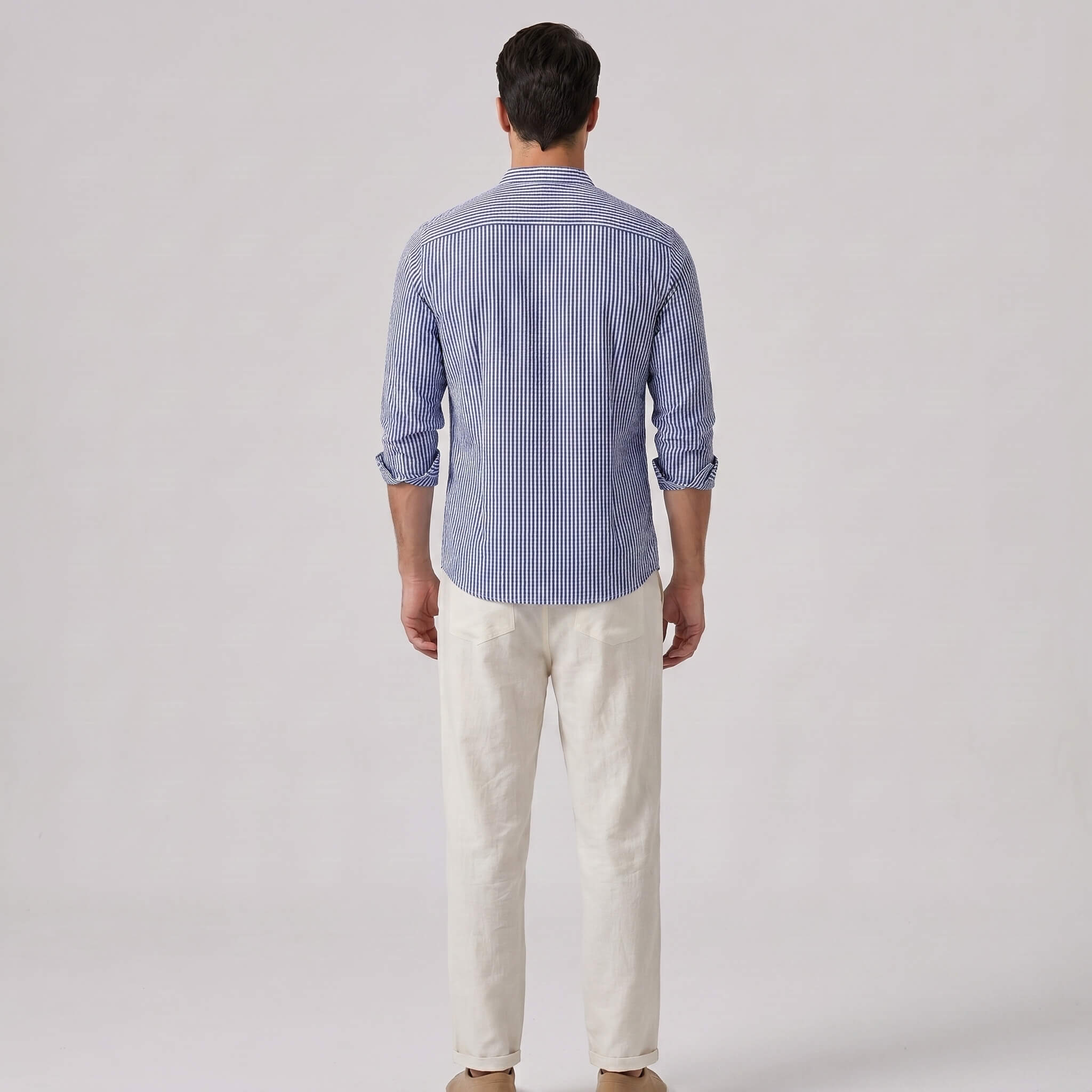 Back view of man wearing a blue striped shirt and white pants on a gray background
