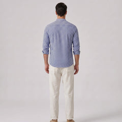 Back view of man wearing a blue striped shirt and white pants on a gray background