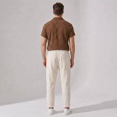 Back view of man wearing a brown patterned shirt and beige pants against a plain background