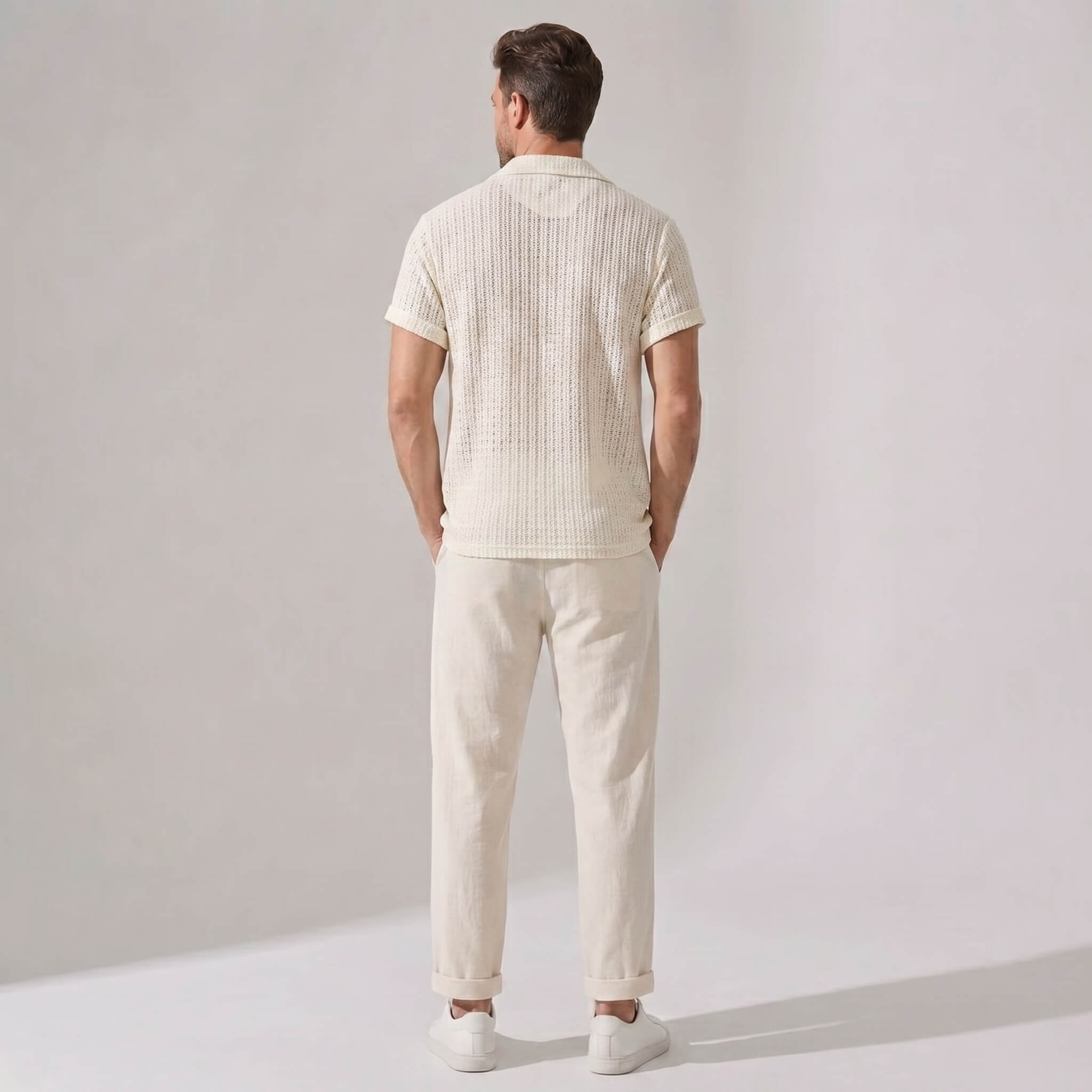 Back view of man wearing a cream-colored outfit with a shirt and pants on a plain background