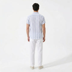 Back view of man wearing a light blue striped shirt and white pants on a white background
