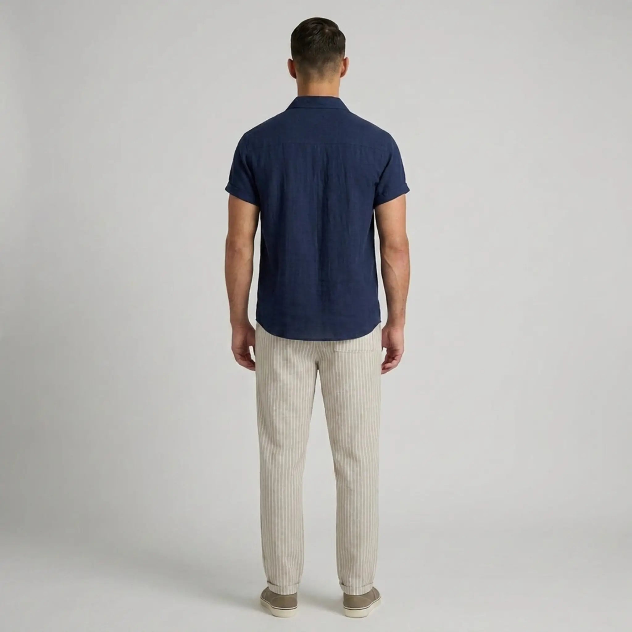 Back view of man wearing a navy blue polo shirt and beige striped pants on a light gray background