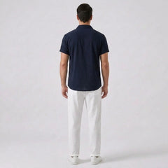 Back view of man wearing a navy polo shirt and white pants on a light gray background