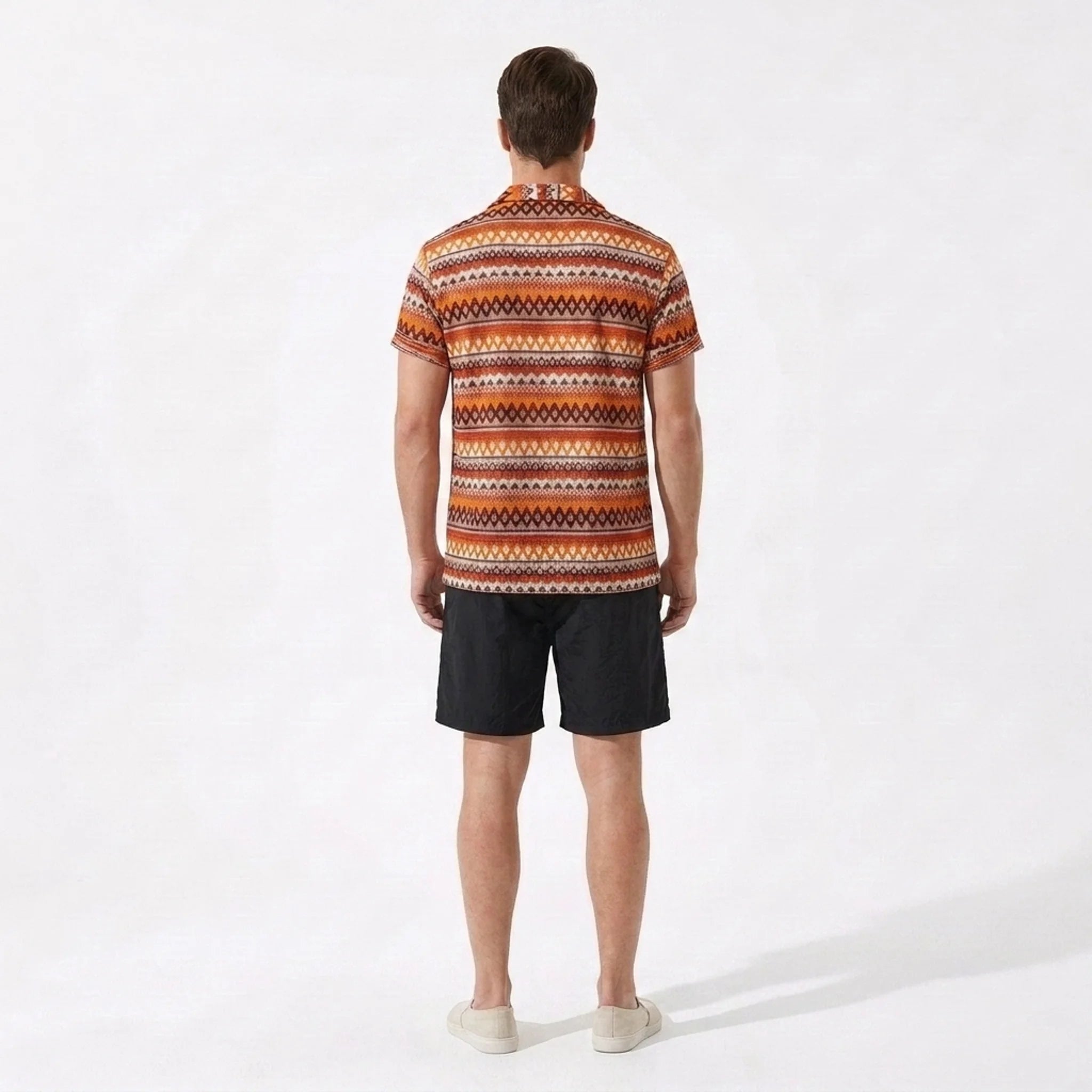 Man wearing a patterned shirt and black shorts on a white background