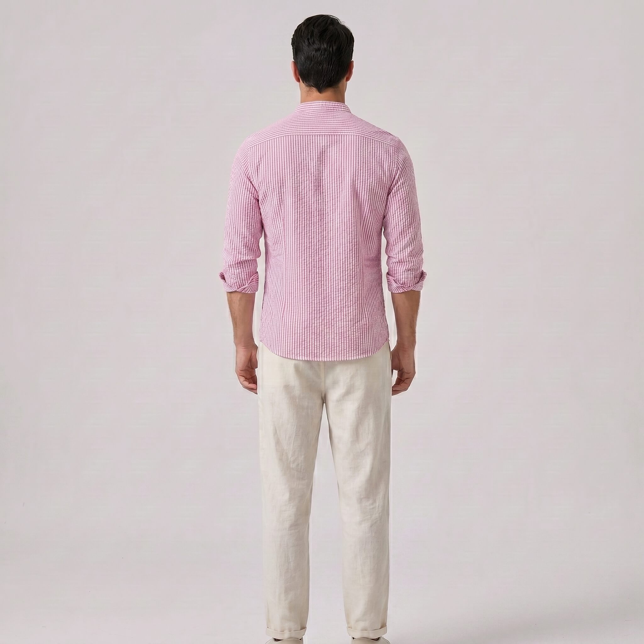 Back view of man wearing a pink checkered shirt and white pants on a light gray background