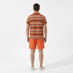 Back view of man wearing an orange and brown patterned shirt with orange shorts on a white background