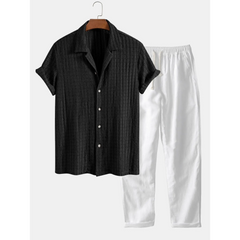 Black short-sleeve shirt and white pants on a hanger against a white background