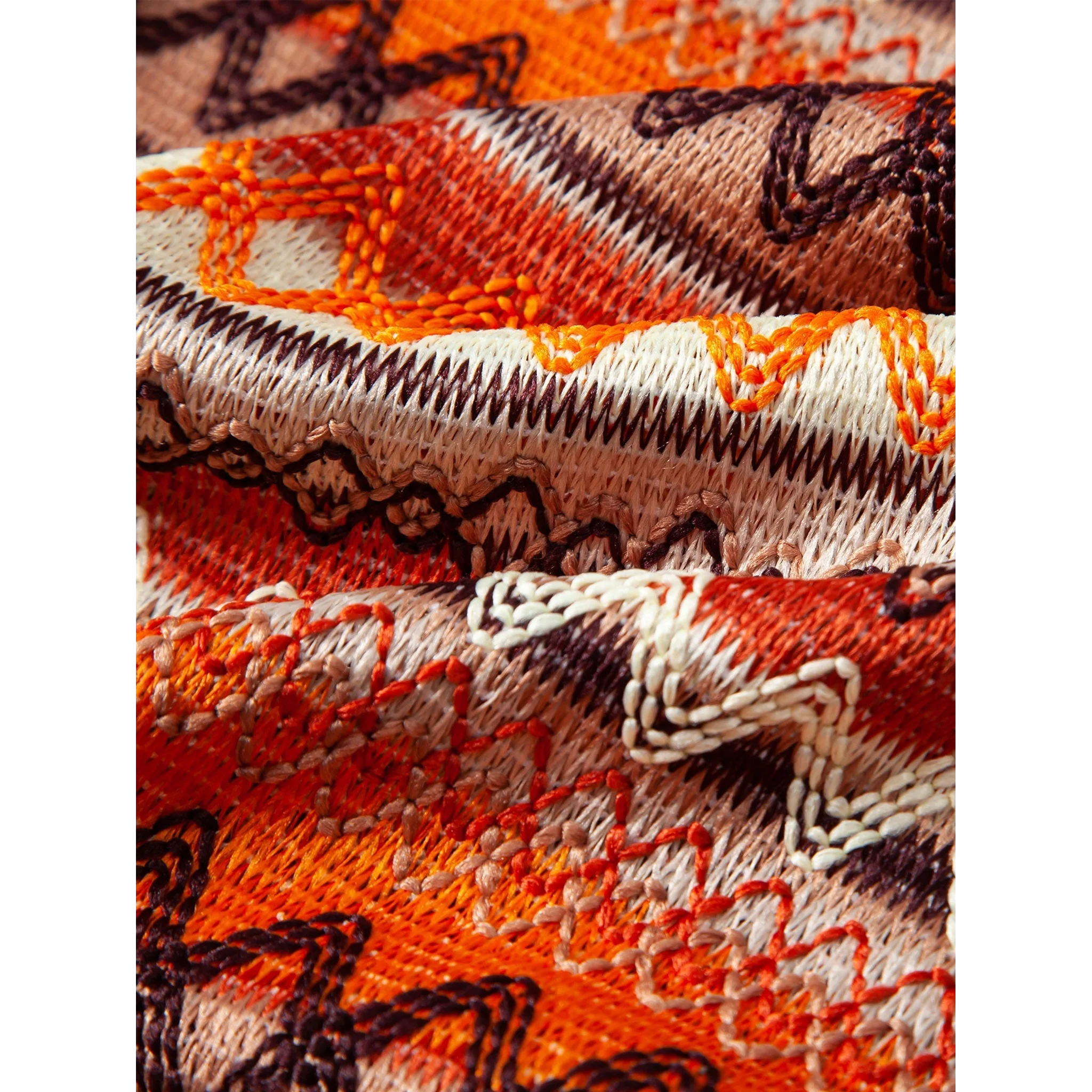 Close-up of embroidered fabric with orange, brown, and beige patterns.