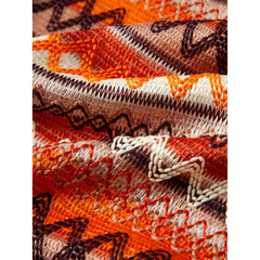Close-up of embroidered fabric with orange, brown, and beige patterns.