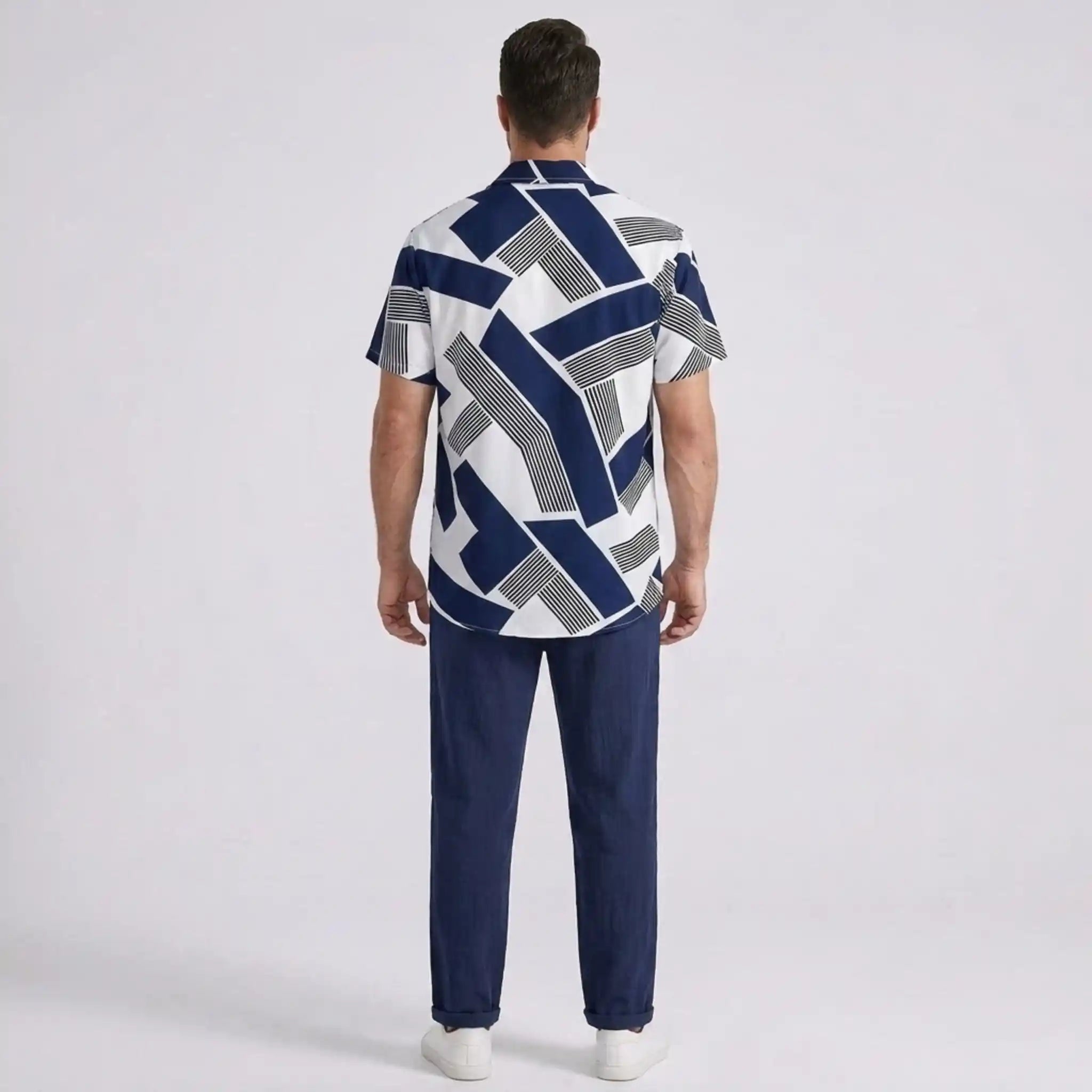 Man back view wearing a patterned shirt and dark pants on a light gray background
