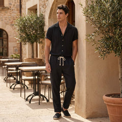 Man in a black outfit standing outdoors near tables and plants