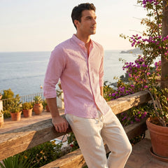 Man in a pink shirt standing by a wooden railing with a scenic ocean view.