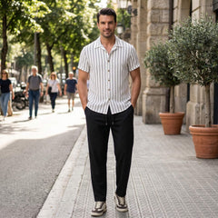 Man in a striped shirt and black pants standing on a city street