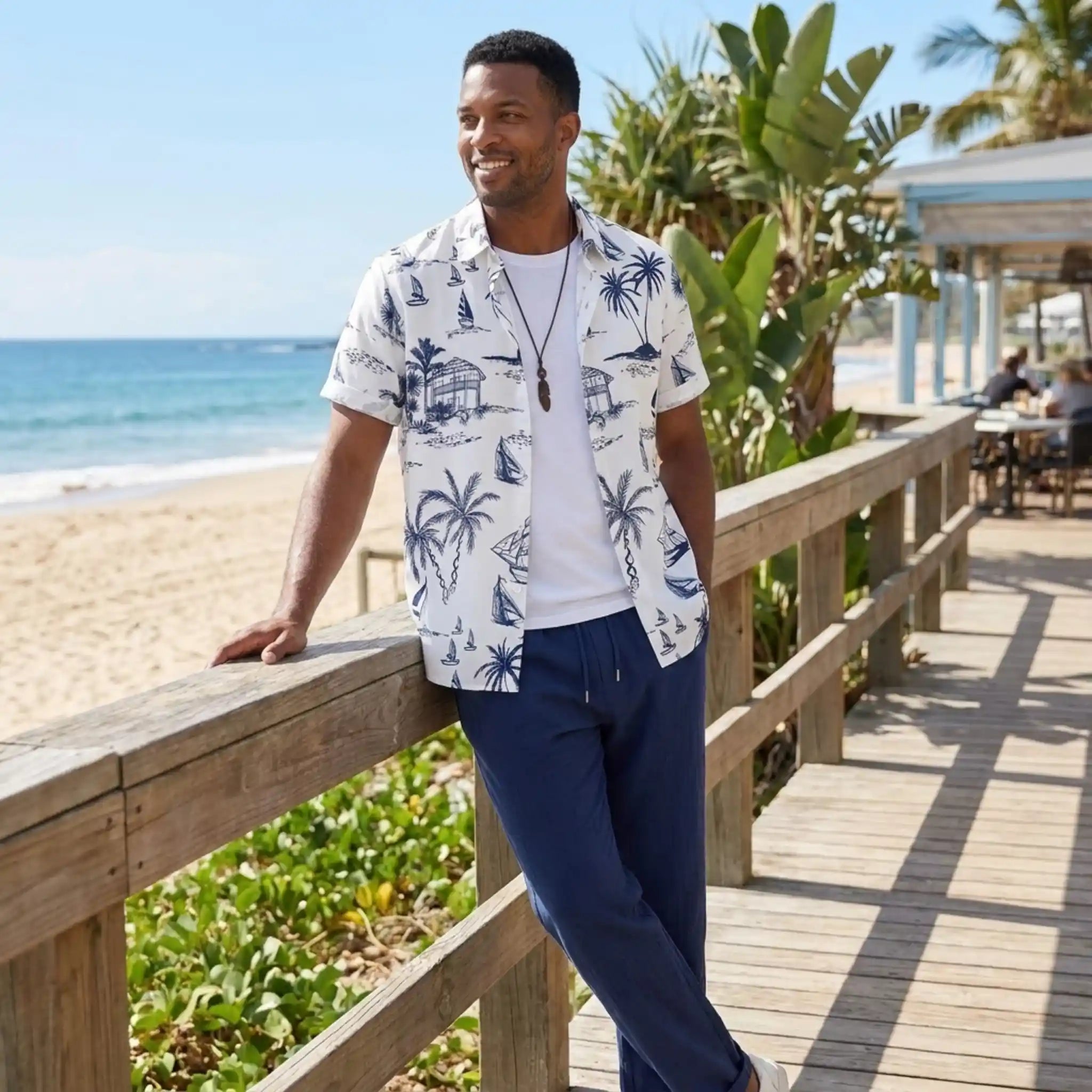 Man in a tropical shirt standing on a wooden deck by the beach