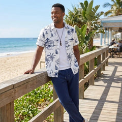 Man in a tropical shirt standing on a wooden deck by the beach
