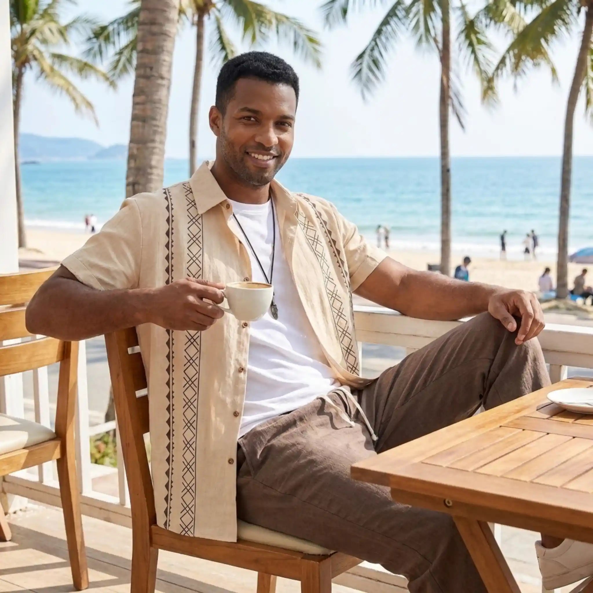 Man in beige outfit sitting on a cafe by a stone wall with potted plants and ocean view