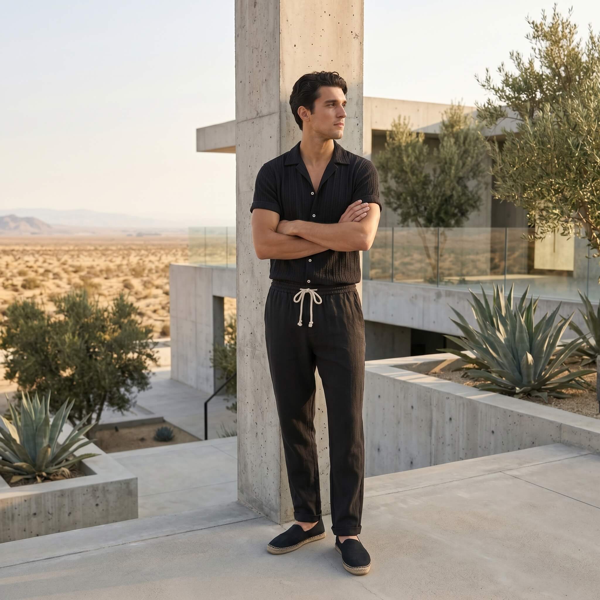 Man in black outfit standing in a modern outdoor setting with concrete structures and desert landscape.