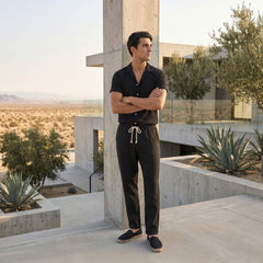 Man in black outfit standing in a modern outdoor setting with concrete structures and desert landscape.