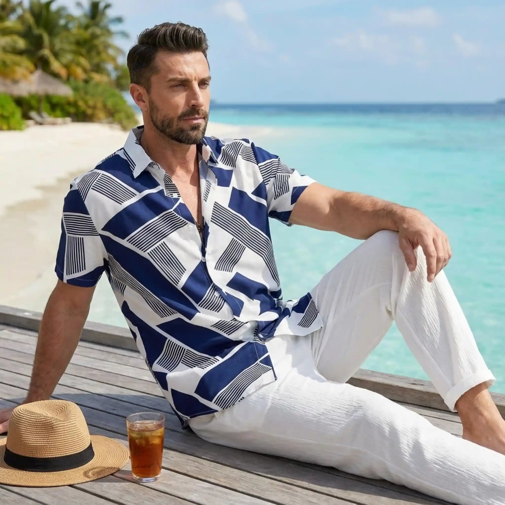 Man in blue pattern shirt with white trouser sitting by the sea.