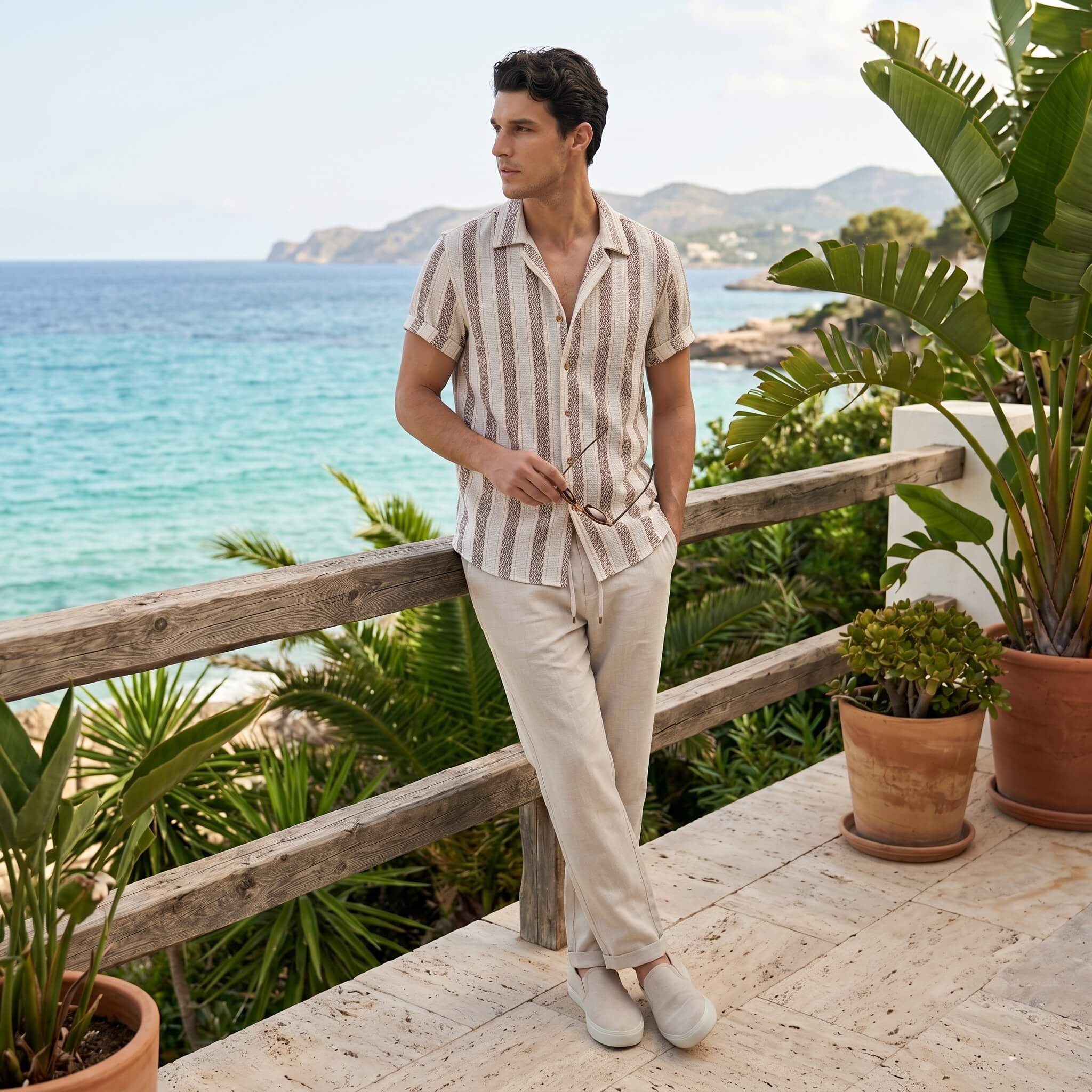 Man in striped shirt and beige pants standing on a wooden deck with ocean view