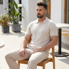 Man sitting on a chair wearing a beige outfit in an outdoor setting.