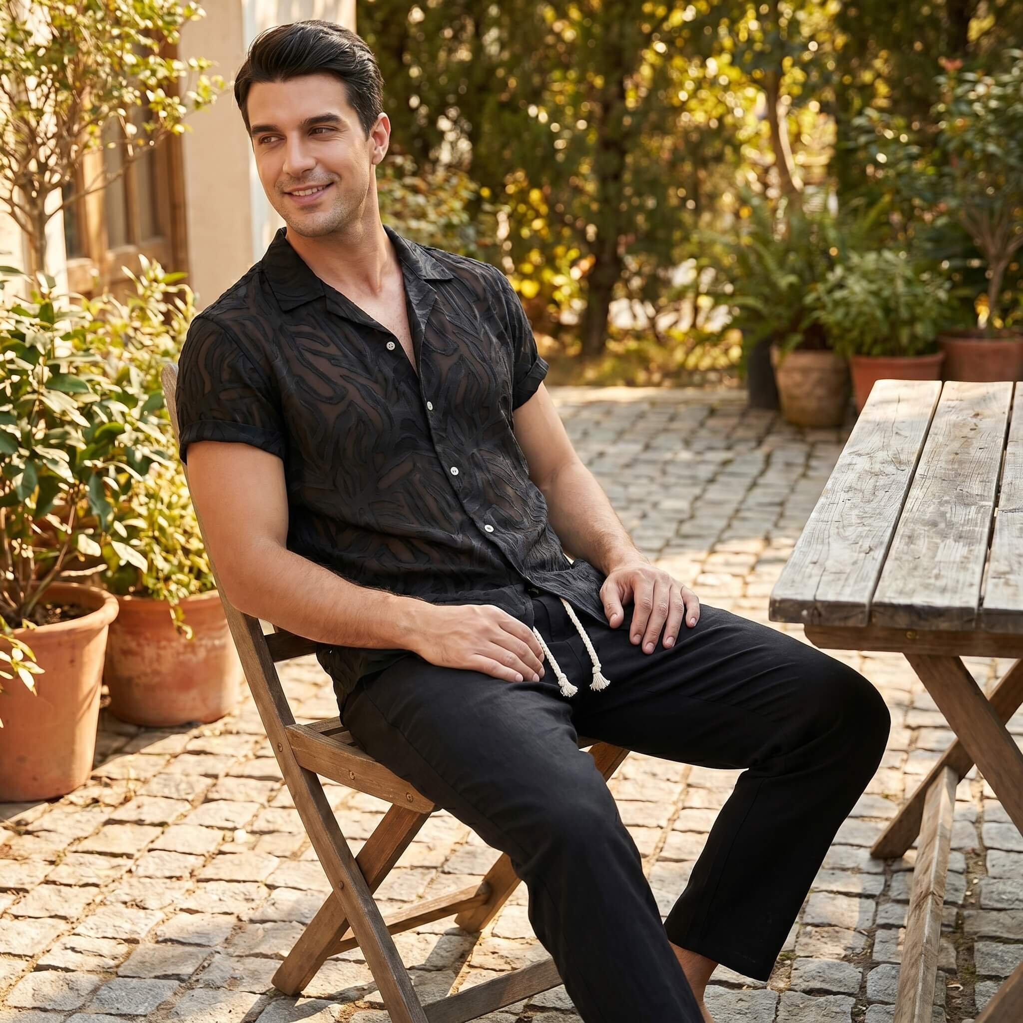 Man sitting outdoors on a wooden chair with plants and a table in the background