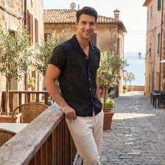 Man standing on a balcony with a scenic view of buildings and ocean.
