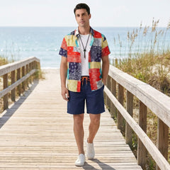 Man standing on a wooden boardwalk by the beach wearing a colorful shirt and navy shorts.